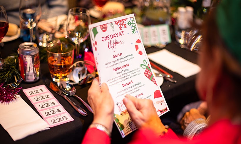 Person reading a food menu at One Day At Christmas. The table is decorated for a Christmas meal.