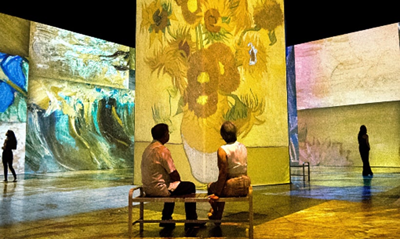 Two people sat on a stool looking at a sunflower projection at Beyond Van Gogh.