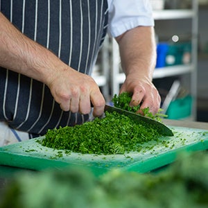 A chef cutting herbs on a chopping board.