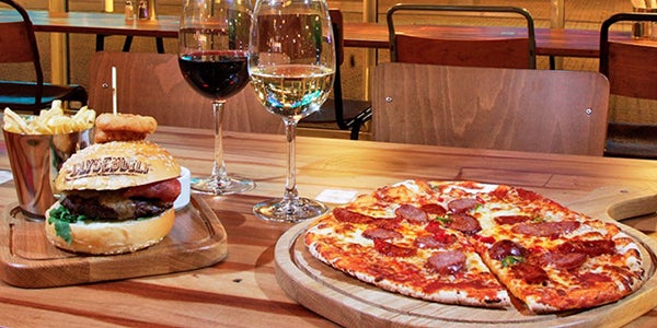 Two meals on a table in Clydebuilt consisting of a burger and chips, pizza, a glass of red white and a glass of white wine.