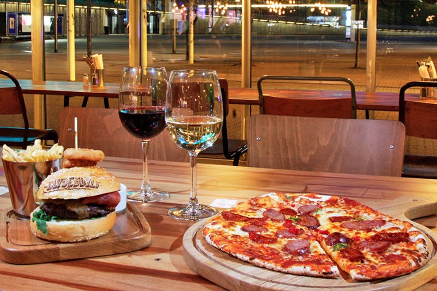 Two meals on a table in Clydebuilt consisting of a burger and chips, pizza, a glass of red white and a glass of white wine.