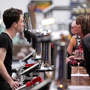Man serving woman in clydebuilt over a various drink taps.