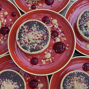 Numerous plates of a chocolate tart with compote on the side.