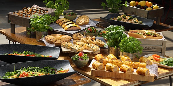 A variety of food dishes on a table. The various dishes include breads, salads, keish, scotch eggs, baguettes and fruit.