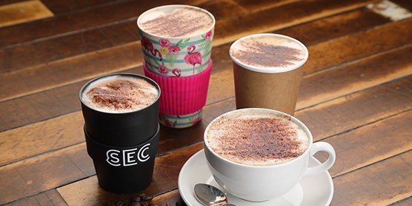 Travel cups and mug of coffee with chocolate sprinkled on top.