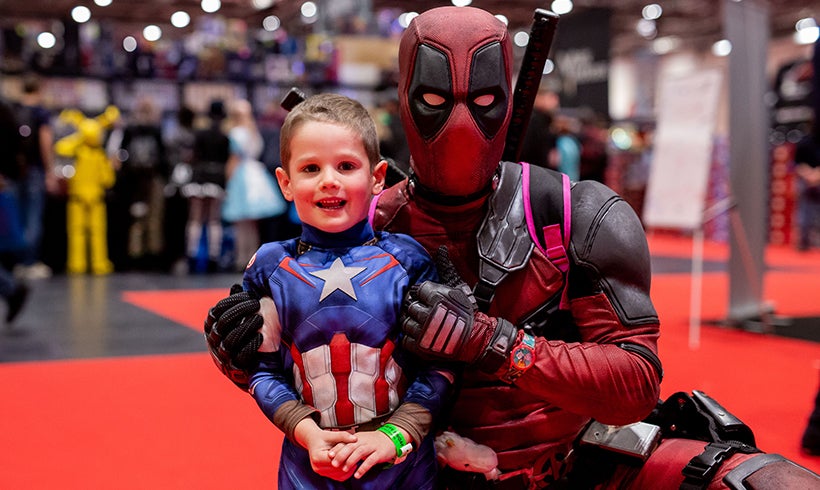 Person dressed up as Deadpool posing for picture with young boy dressed up at super hero.