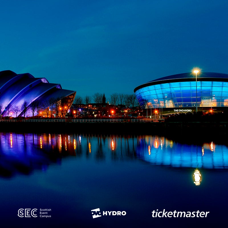 View of the OVO Hydro and SEC Armadillo from the River Clyde. The OVO Hydro has been lit up blue and the SEC Armadillo has been lit up Purple. OVO Hydro, SEC Armadillo and Ticketmaster assets are at the bottom of this image.