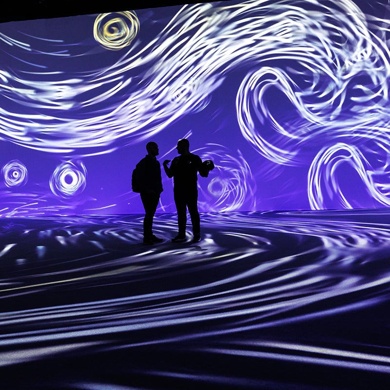 People in front of a purple swirly projection at Beyond Van Gogh.