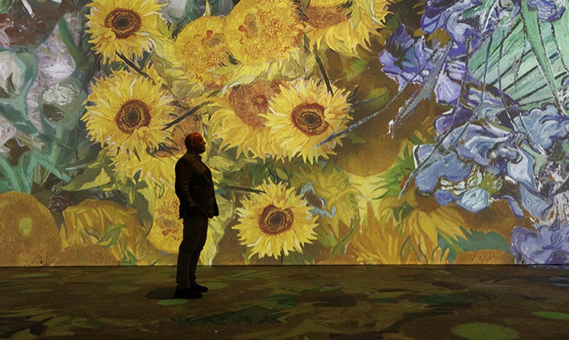 Person in front of a sunflower projection at Beyond Van Gogh exhibition.