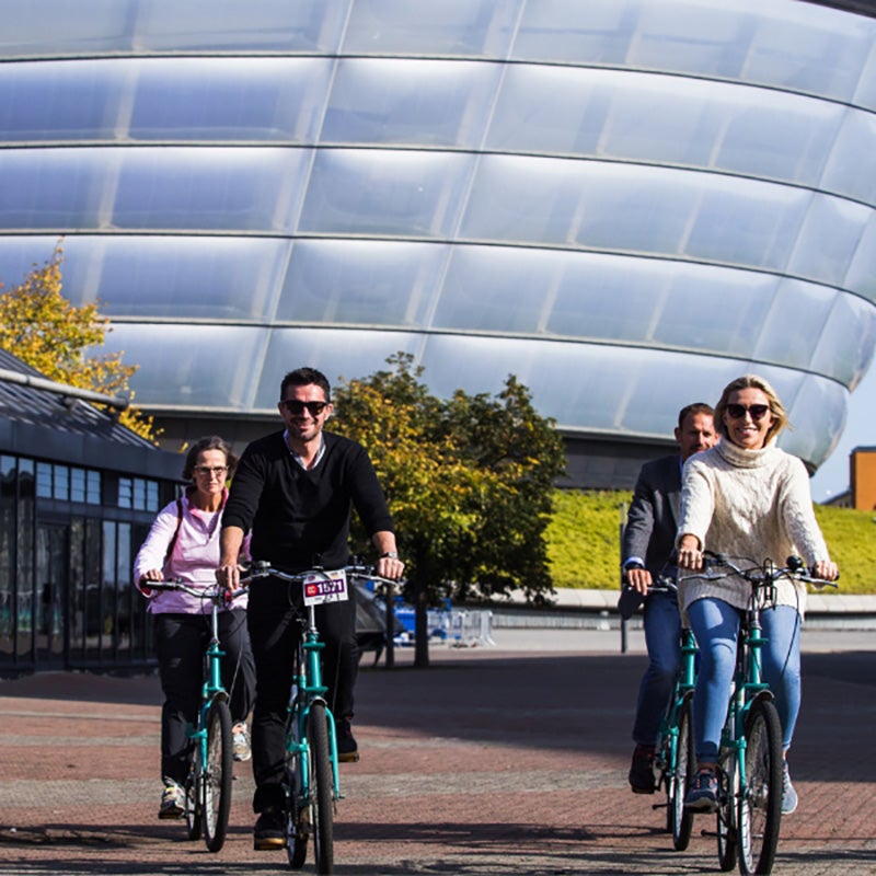 People cycling in front of the OVO Hydro.
