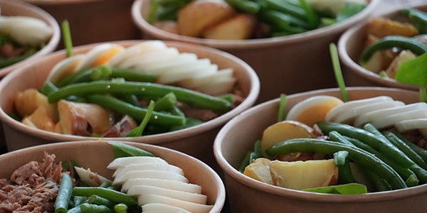 Carboard bowls off food with various ingredients such as eggs, tuna, potatoe and green beans.