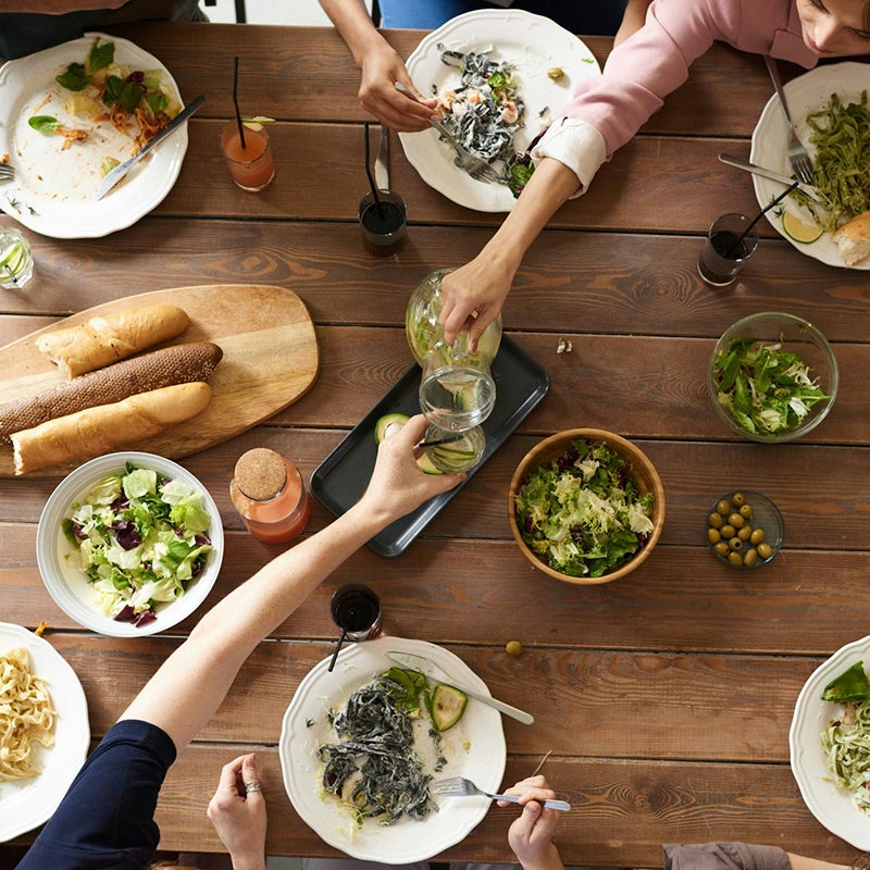 Two people taking food and drink from a spread on a wooden table.
