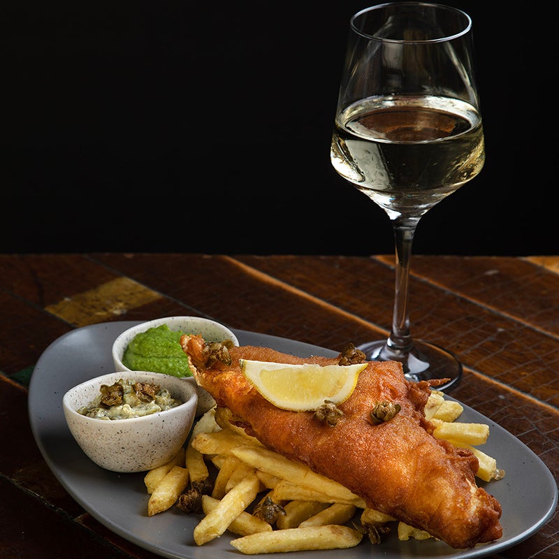 Fish and chips and a glass of wine on a table with a dark background.