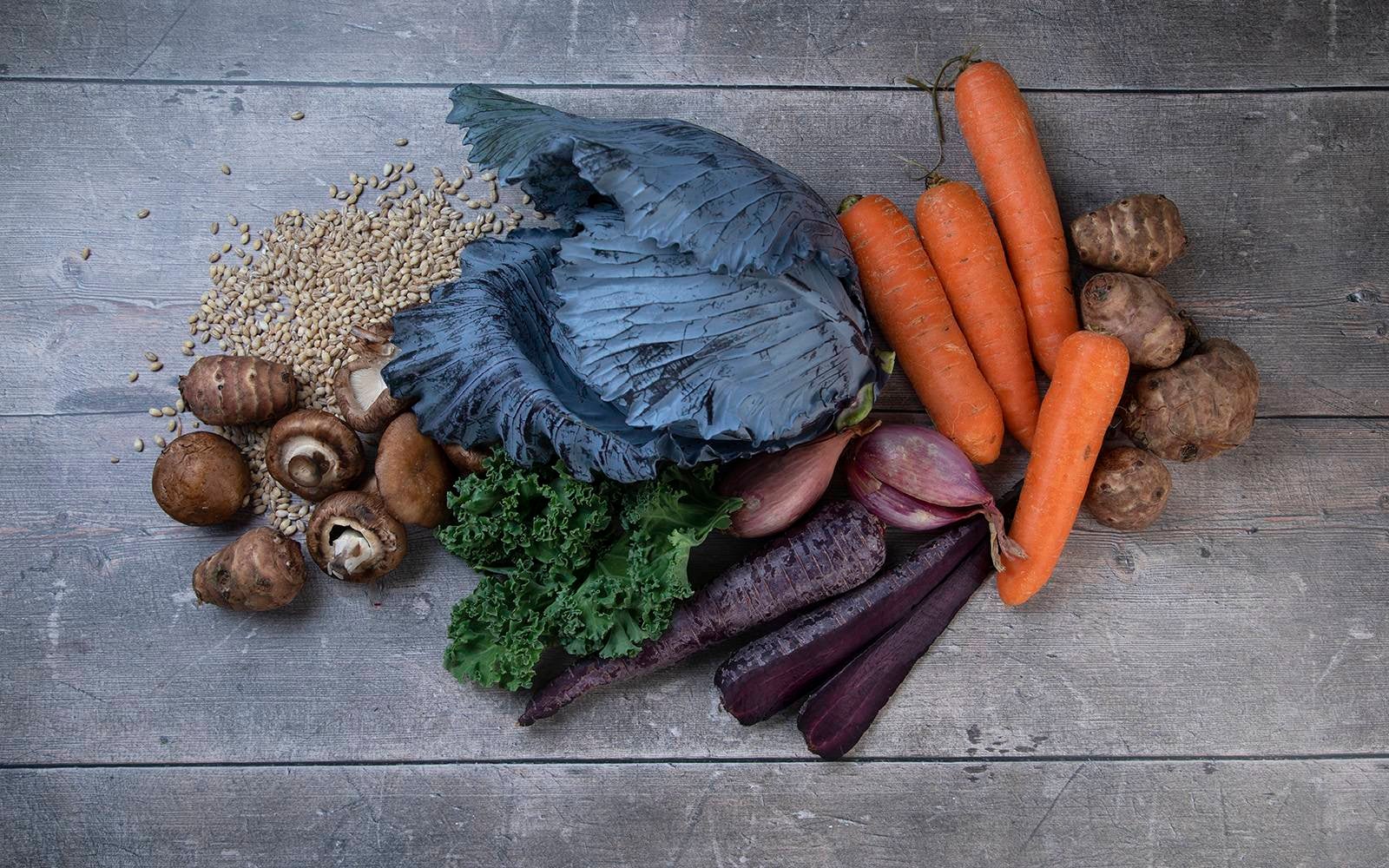 Birdseye view of a wooden table with vegetable on top such as carrots, mushrooms, shallots and kale.