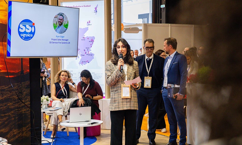 Woman presenting in front of a screen at a trade exhibition.