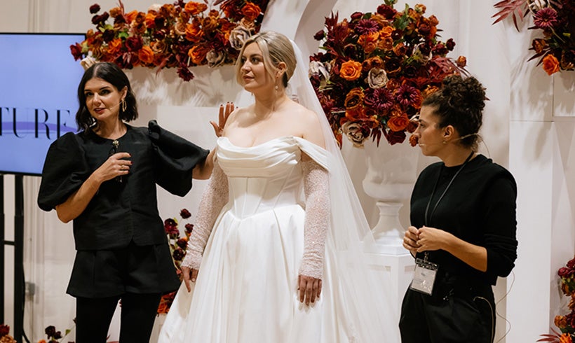 Woman modelling a wedding dress whilst two other ladies talk about the dress.